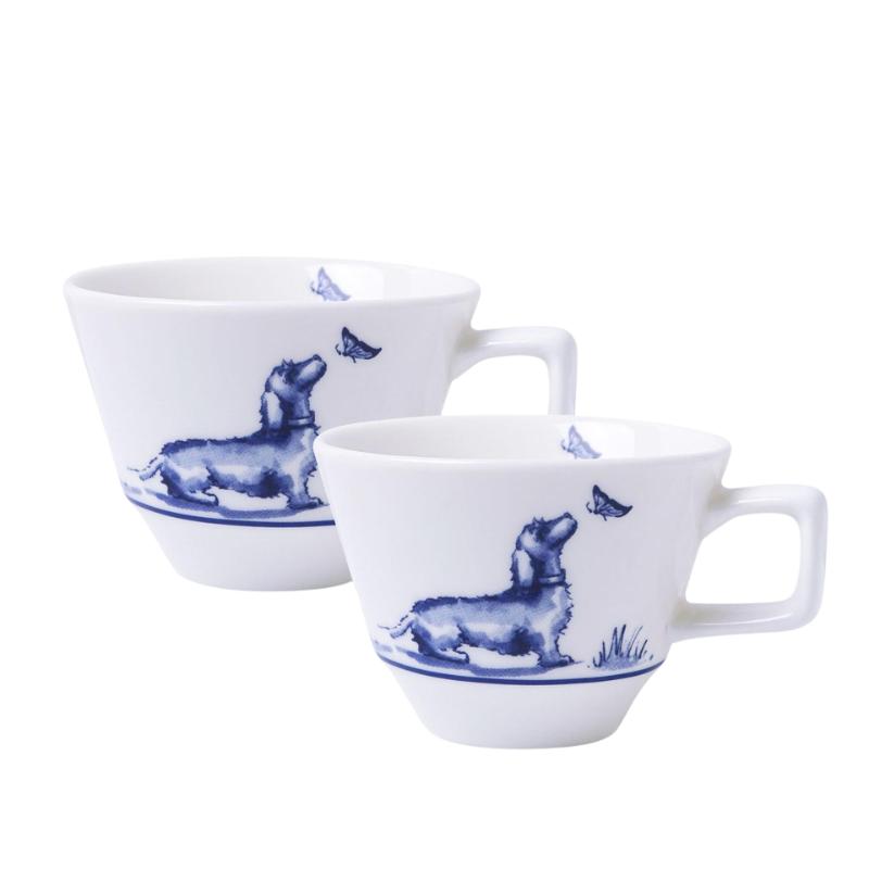 Zwei weiße Espressotassen mit einem blau illustrierten Dackel, der auf einer Wiese sitzt und einen Schmetterling betrachtet, umgeben von einem dekorativen blauen Rand.