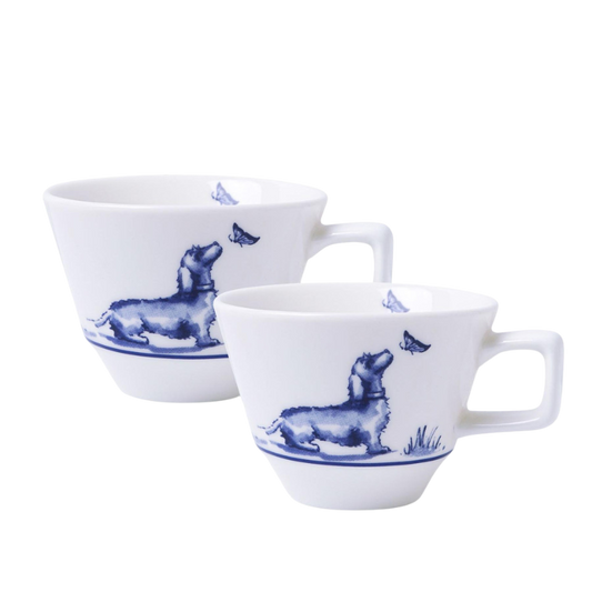 Zwei weiße Espressotassen mit einem blau illustrierten Dackel, der auf einer Wiese sitzt und einen Schmetterling betrachtet, umgeben von einem dekorativen blauen Rand.