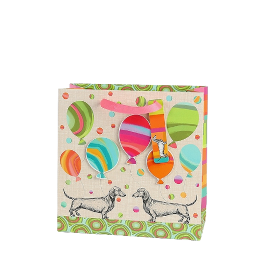 Bunte Geschenktasche mit Dackel-Illustrationen, farbenfrohen Ballons und rosa Trageschlaufe, verziert mit verspieltem Punkt- und Kreismuster.