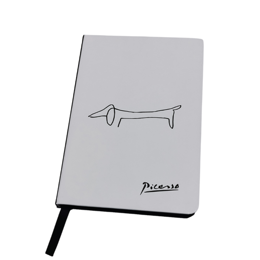 Ein weißes Notizbuch mit einem minimalistischen schwarzen Dackel-Motiv, inspiriert von Picasso, und Picasso’s Signatur in der Ecke.