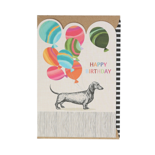 Geburtstagskarte mit einem gezeichneten Dackel, der bunte Ballons am Rücken trägt, daneben der bunte Schriftzug „Happy Birthday“