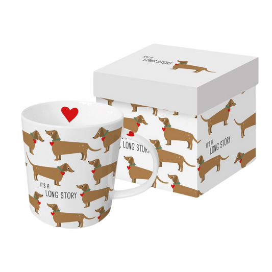 Weißer Keramikbecher bedruckt mit mehreren Dackeln, die Schleifen tragen und den Text ‘It’s a long story’ tragen, verpackt in einer weißen Geschenkbox mit einem roten Herz auf dem Becher.