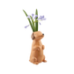 vase in Form eines sitzenden, fröhlich dreinblickenden Dackels. Aus dem Kopf der Figur ragen lila Blüten und grüne Blumenstängel wie aus einer klassischen Vase.