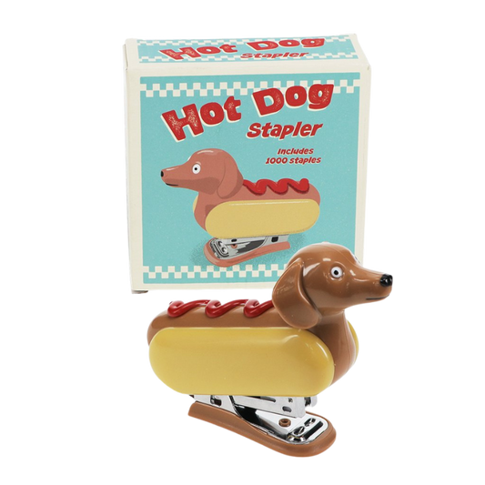 Witziger Klammerhefter im Stil eines Hot Dogs mit Dackelkopf. Der Hefter hat einen gelben „Brötchen“-Körper, eine rote Ketchup-Linie oben und ein süßes Dackelgesicht. Büroklammern liegen daneben.