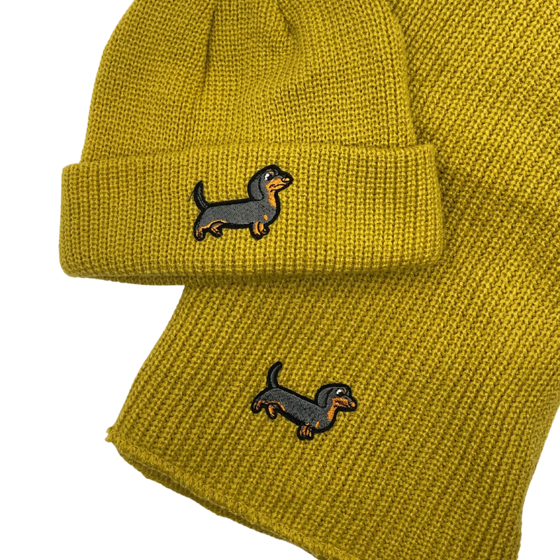 Gelbes Strick-Set bestehend aus Mütze und Schal, beide mit aufgesticktem Dackel-Motiv.