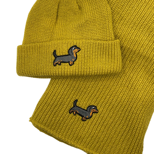 Gelbes Strick-Set bestehend aus Mütze und Schal, beide mit aufgesticktem Dackel-Motiv.