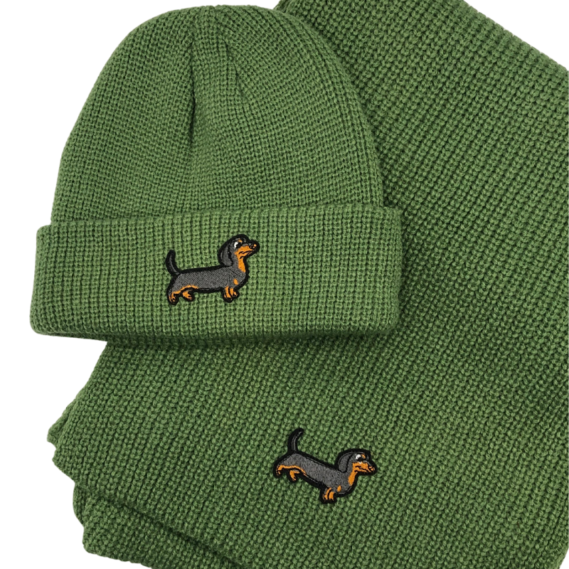 Grünes Strick-Set bestehend aus Mütze und Schal, verziert mit einem gestickten Dackel-Motiv.