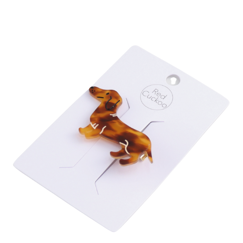 Haarklammer in Form eines Dackels aus braun gemustertem Acryl mit goldfarbener Metallklammer auf der Rückseite. Das Design zeigt den Dackel in Seitenansicht mit niedlichen Details wie Ohr und Rute.