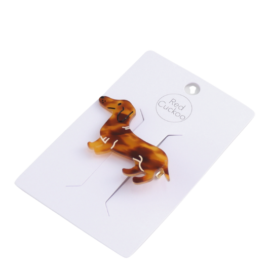 Haarklammer in Form eines Dackels aus braun gemustertem Acryl mit goldfarbener Metallklammer auf der Rückseite. Das Design zeigt den Dackel in Seitenansicht mit niedlichen Details wie Ohr und Rute.