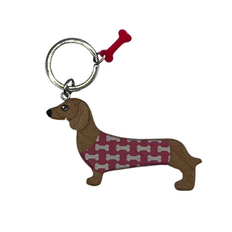 Holz-Schlüsselanhänger in Form eines Dackels mit bordeauxfarbenem Pullover mit weißen Knochenmotiven und pinkem Knochen-Anhänger am Schlüsselring.