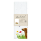 Weißes Geschirrtuch mit Aquarell-Illustration eines braunen Dackels, der durch eine bunte Blumenwiese läuft; im Vordergrund gelbe und rote Blüten sowie ein flatternder Schmetterling. Verpackt mit Papierbanderole.