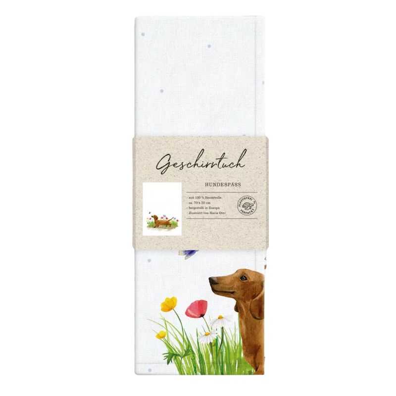 Weißes Geschirrtuch mit Aquarell-Illustration eines braunen Dackels, der durch eine bunte Blumenwiese läuft; im Vordergrund gelbe und rote Blüten sowie ein flatternder Schmetterling. Verpackt mit Papierbanderole.