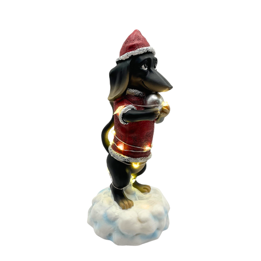 Weihnachtsdeko-Figur eines Dackels im roten Weihnachtsmann-Outfit mit Lichterkette und Geschenk in der Pfote.