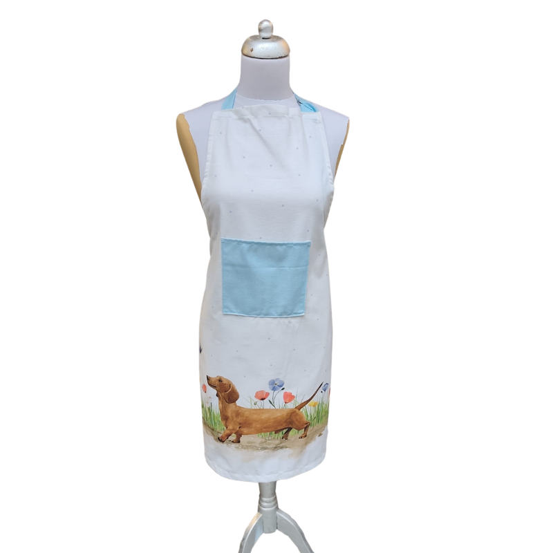 Weiße Küchenschürze mit hellblauer Tasche und Aquarell-Illustration eines braunen Dackels, der durch eine Blumenwiese läuft; getragen auf einer Schneiderpuppe