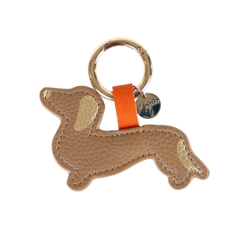 Schlüsselanhänger in Dackelform aus beigefarbenem Leder mit goldenen Details an Ohr und Rute, befestigt an einem goldenen Schlüsselring mit orangener Schlaufe und rundem Anhänger.