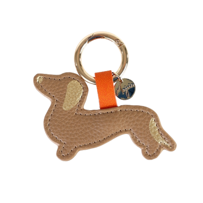 Schlüsselanhänger in Dackelform aus beigefarbenem Leder mit goldenen Details an Ohr und Rute, befestigt an einem goldenen Schlüsselring mit orangener Schlaufe und rundem Anhänger.