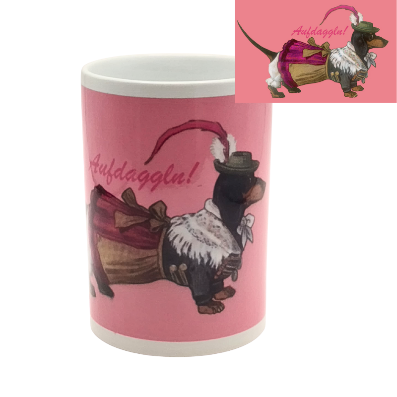 Weiße Tasse mit pinkem Hintergrund und Aufdruck eines Dackels in bayerischer Tracht, der ein Dirndl trägt und mit dem Spruch „Aufdaggl’n!“ versehen ist.
