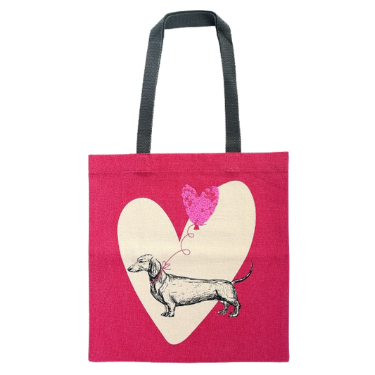 Rosa Tragetasche mit schwarzem Henkel, bedruckt mit einem gezeichneten Dackel vor einem großen cremefarbenen Herz und einem pinken Herzluftballon aus Pailletten