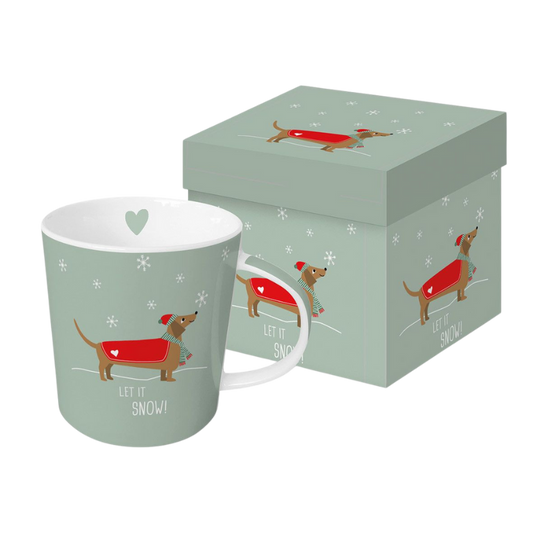 Hellgrüne Porzellantasse mit Weihnachtsmotiv eines Dackels im roten Mantel, Mütze und Schal, umgeben von Schneeflocken und dem Schriftzug „Let it Snow!“, inklusive passender Geschenkverpackung mit gleichem Design.