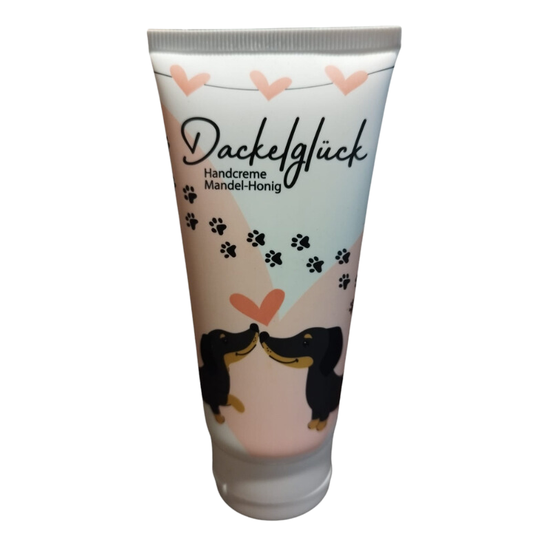 Tube der ‘Dackelglück’ Handcreme in sanften Pastelltönen mit einem romantischen Dackelmotiv, das zwei Dackel zeigt, die sich an einem rosa Herzen schnuppern, umgeben von schwarzen Pfotenabdrücken und Herzen, Text “Handcreme Mandel-Honig” auf der Tube.